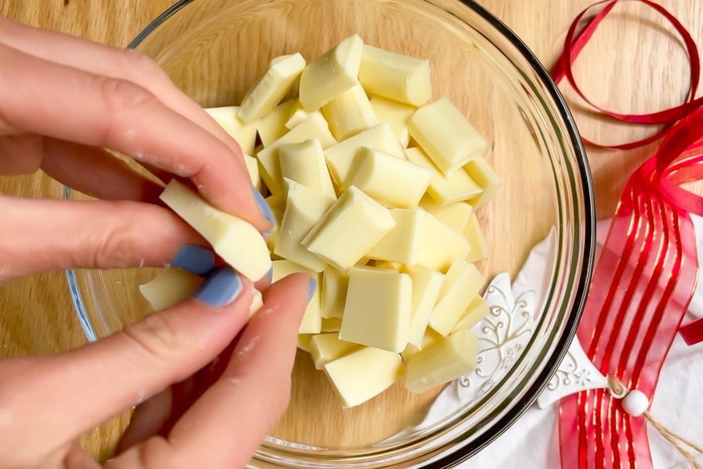 hands breaking up white chocolate into a heatproof bowl ready to melt