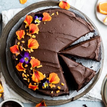 overhead photo of chocolate orange cake with two slices of cake cut out and one slice on a plate in the lower right corner.
