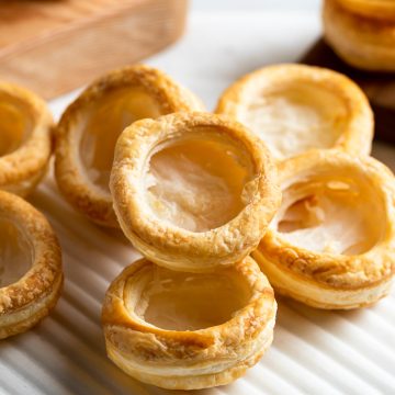 baked golden vol-au-vent cases on a white board, some stacked on top of each other. Ready to fill.