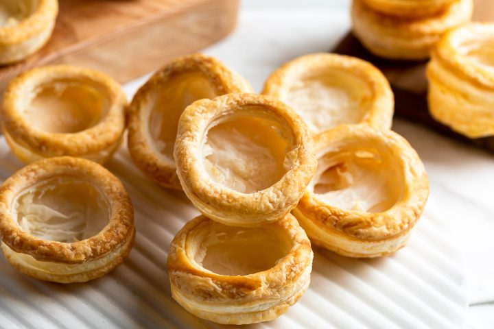 baked golden vol-au-vent cases on a white board, some stacked on top of each other. Ready to fill.
