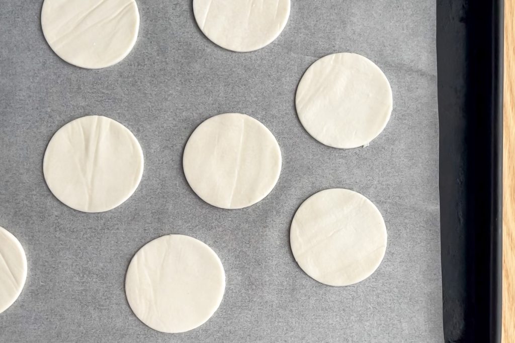 larger circles of puff pastry places on lined baking tin