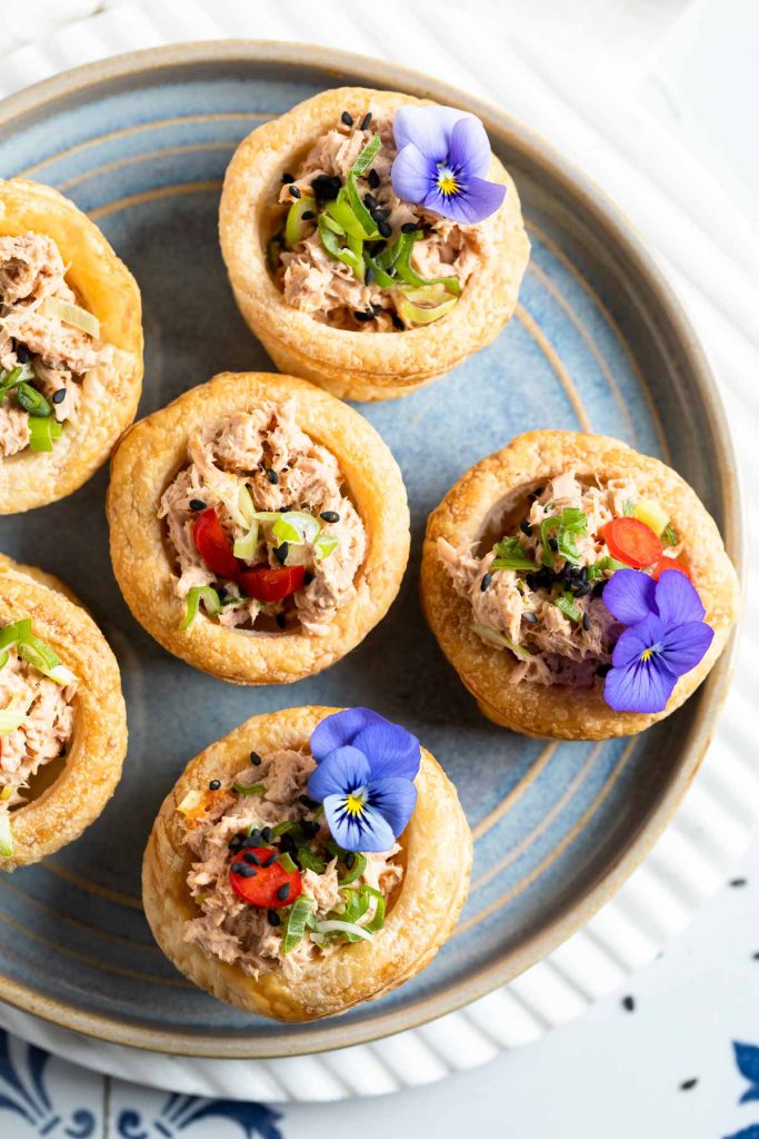 a blue plate topped with vol-au-vents on filled with tuna and decorated with edible purple flowers