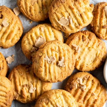 A batch of baked caramilk cookies stacked haphazardly on a baking tray