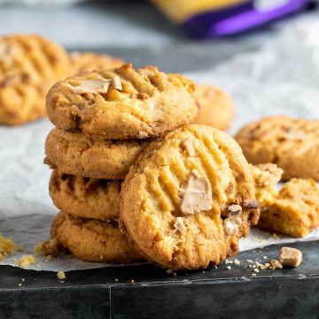 stack of Caramilk cookies, with one cookie leaning against the stack to show the melted caramilk chunks