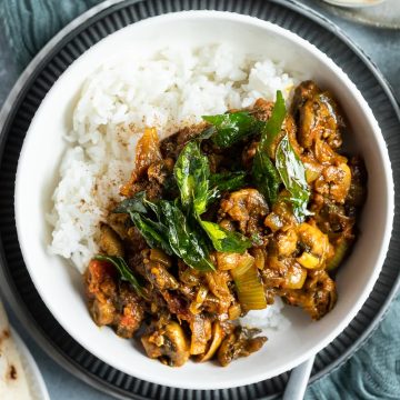mushroom bhaji served in a white bowl with rice and topped with curry leaves, naan bread to one side and a small bowl of pickle to the other