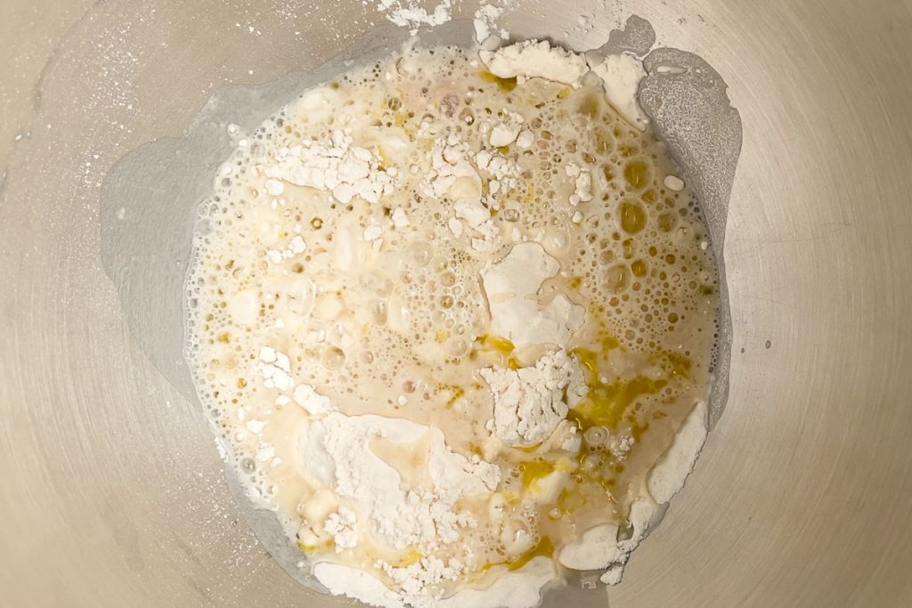 flour, yeast, water and oil in the bottom of a mixer bowl ready to knead.
