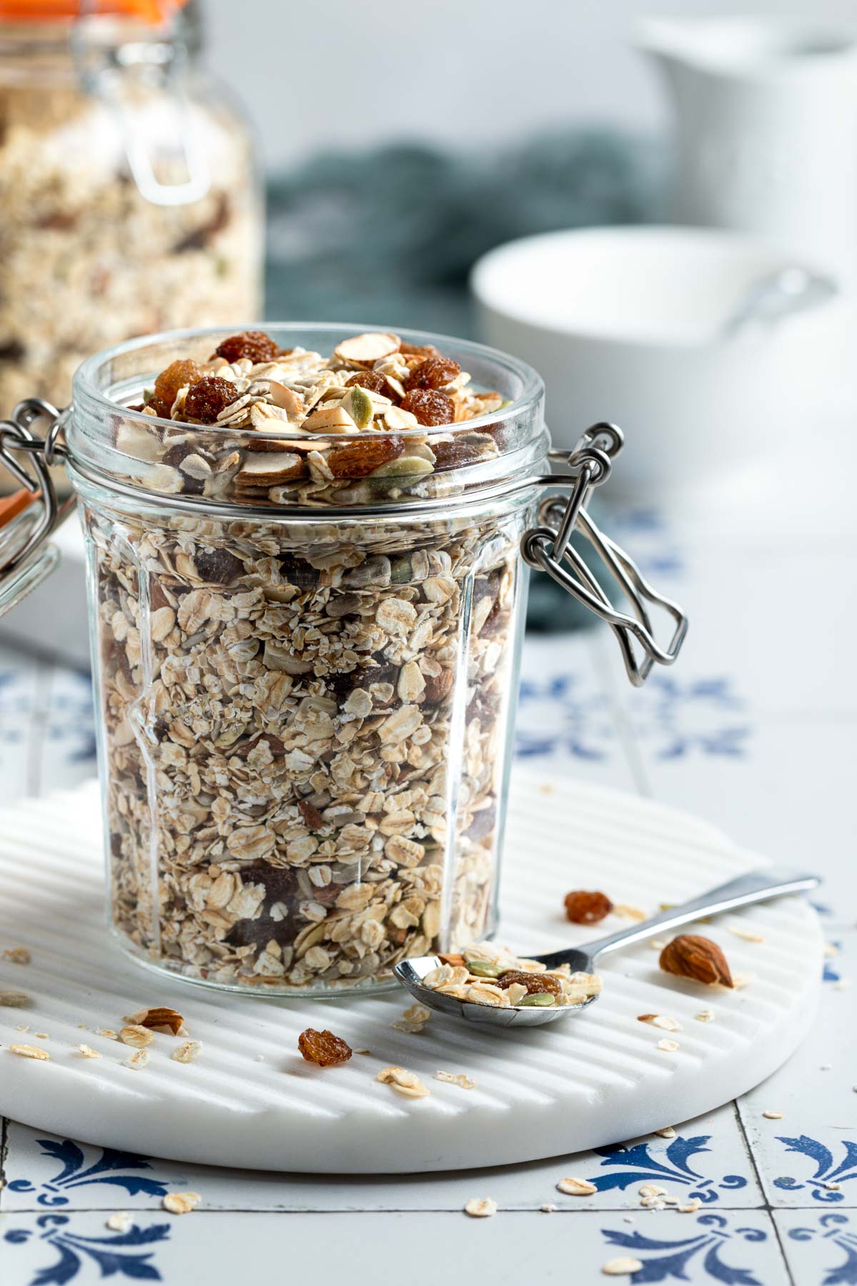 side view of muesli in a storage jar, cereal bowls and spoons just visible behind.