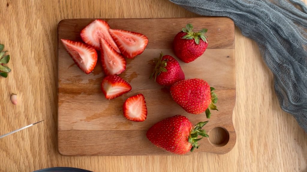 strawberries on a wooden chopping board, larger ones chopped in quarters, smaller ones chopped in half