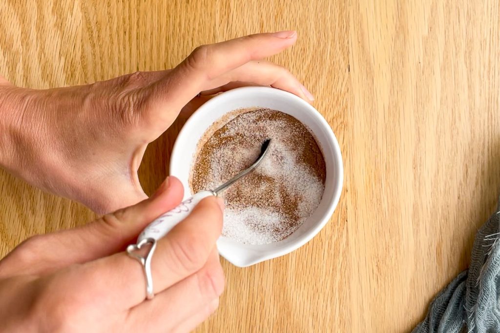 mixing sugar and ground cinnamon together in a small bowl with a spoon.