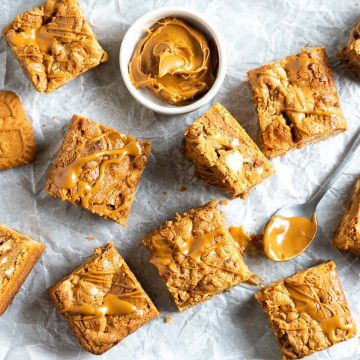 squares of Biscoff Blondies on a tray with Lotus Biscoff biscuits and a small pot of Biscoff cookie butter