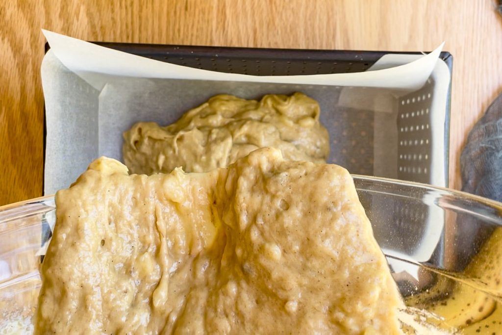 the banana bread batter being poured into a lined loaf tin.