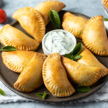 caprese empanadas on a blue plate served with a creamy dip.