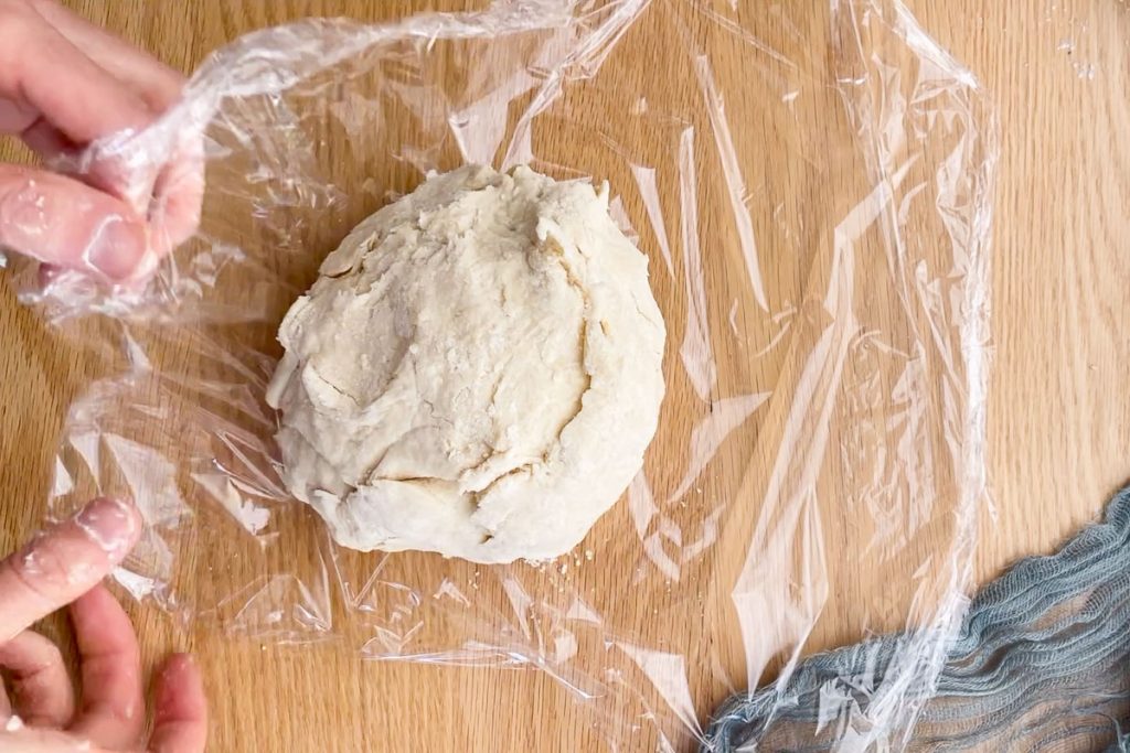 Kneaded empanada dough being wrapped in cling film to rest in the fridge.