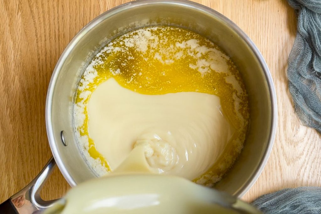 pouring condensed milk into a saucepan of melted butter.