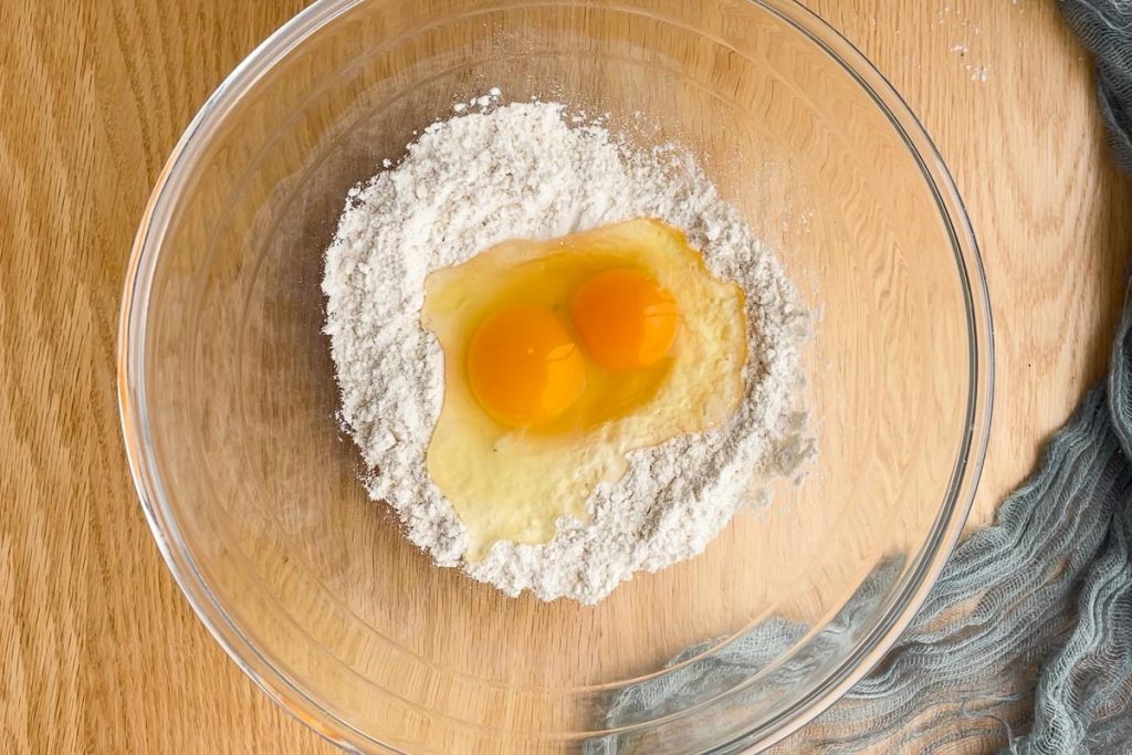 a mixing bowl filled with flour, with two eggs in the well in the flour.