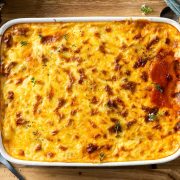 white rectangle dish with cooked lamb pastitsio on a wooden board, side salad just visible in top left corner