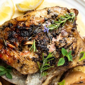 slow cooker lamb shoulder on a white serving plate with lemon wedges and fresh herbs.
