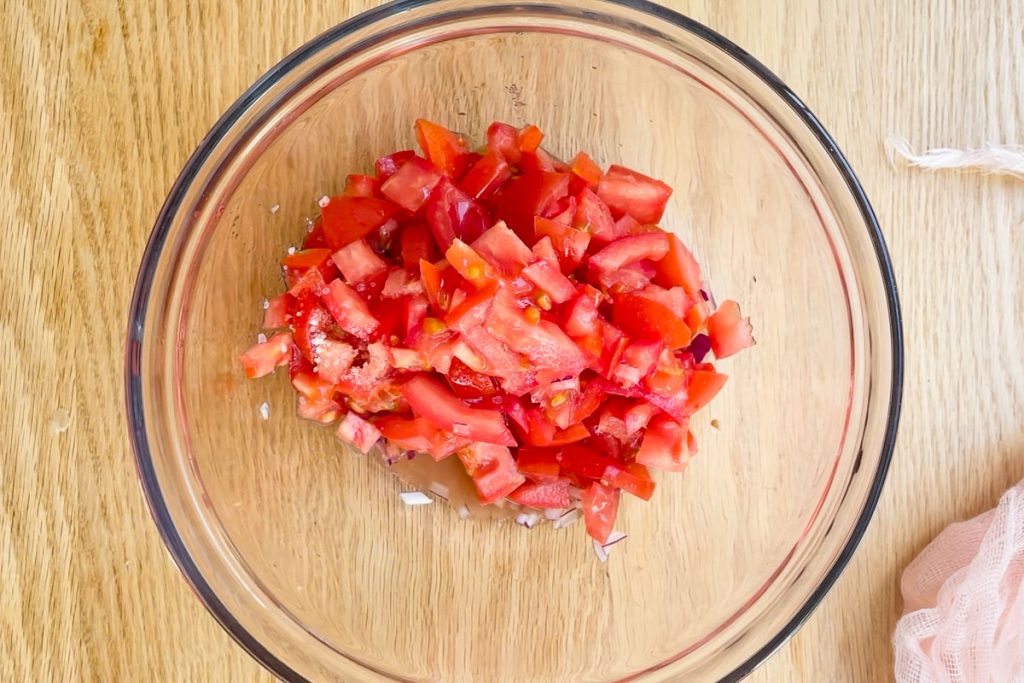 cubed tomatoes, red onion and dressing in a bowl to make tomato salad.