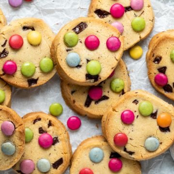 a batch of Smarties cookies on white background, with a small plate of Smarties in the right hand bottom corner.