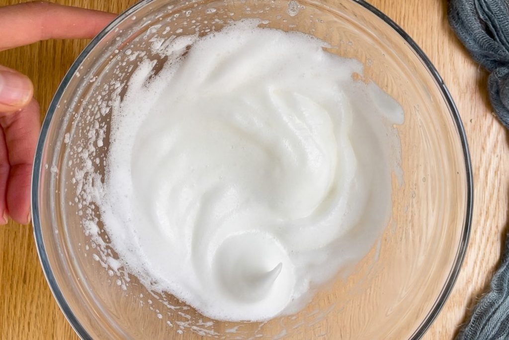 Egg whites in a mixing bowl whisked to a soft peak.
