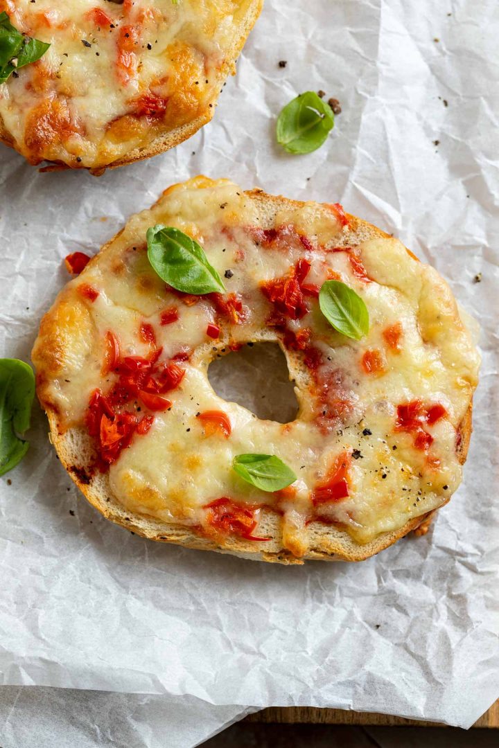 pizza made from a bagel topped with cheese and sprinkled with fresh basil.