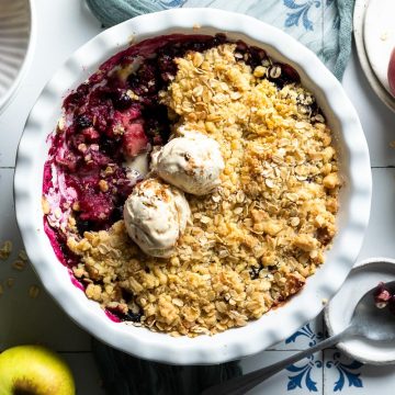 baked blueberry and apple crumble with a portion of the crumble topping taken out to show the fruit filling, topped with scoops of ice cream.