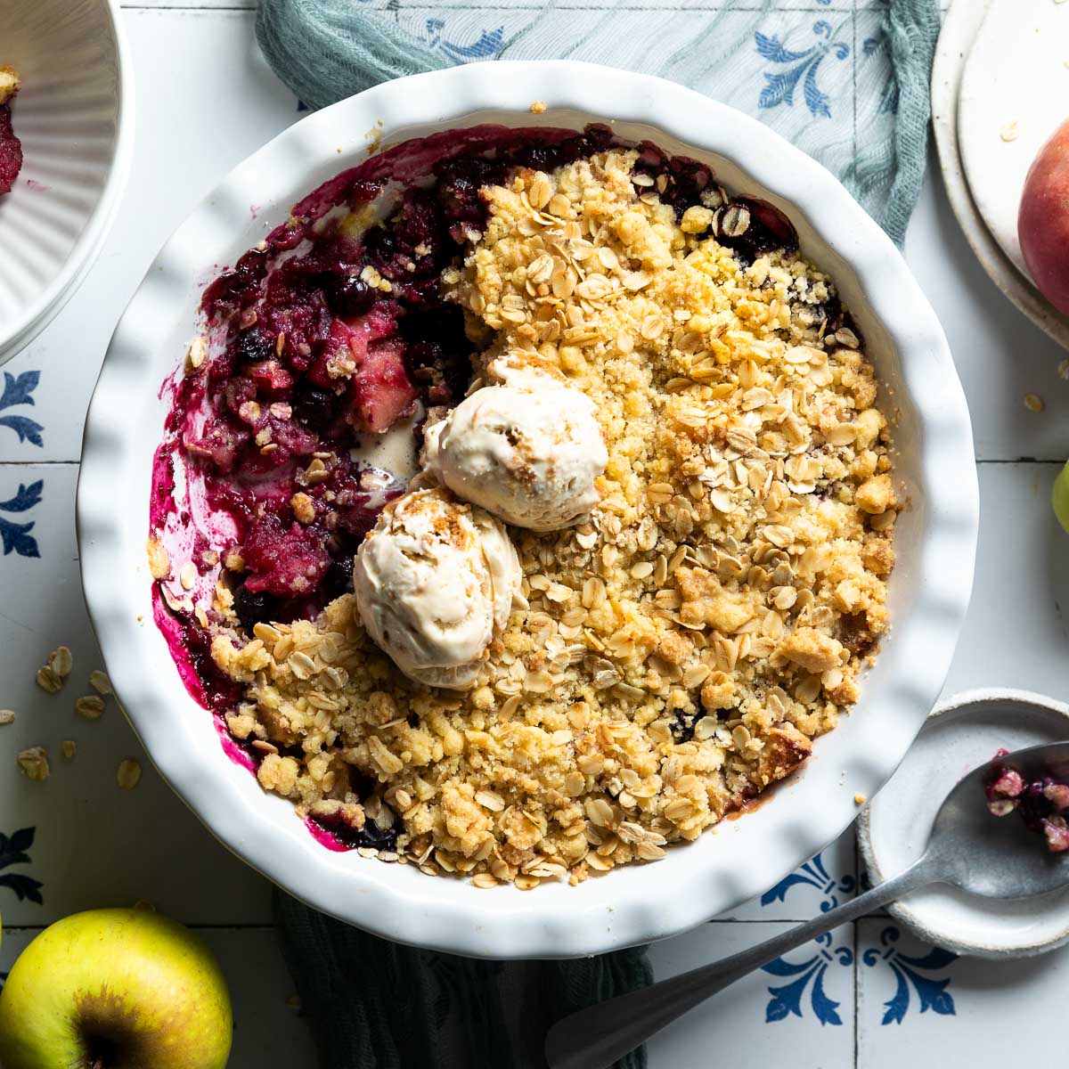 blueberry and apple crumble in white baking dish served with two scoops of ice cream.