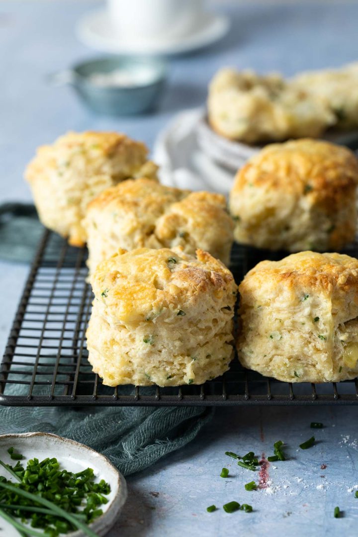 baked chive scones on a metal cooling rack, with chopped fresh scones scattered around the surface.