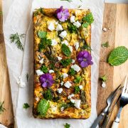 baked silverbeet slice on wooden board sprinkled with fresh herbs and edible flowers.