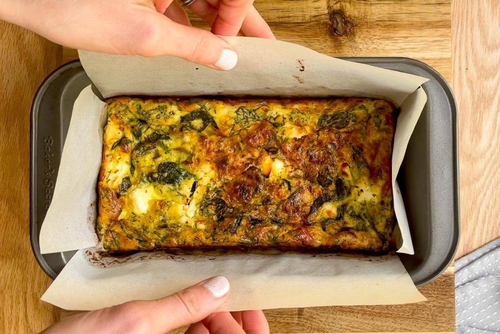 baked slice being lifted out of the tin.