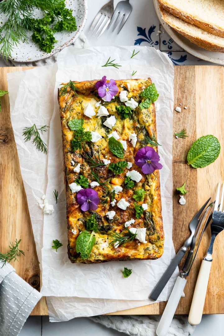 uncut slice on a wooden board decorated with fresh herbs and edible flowers.