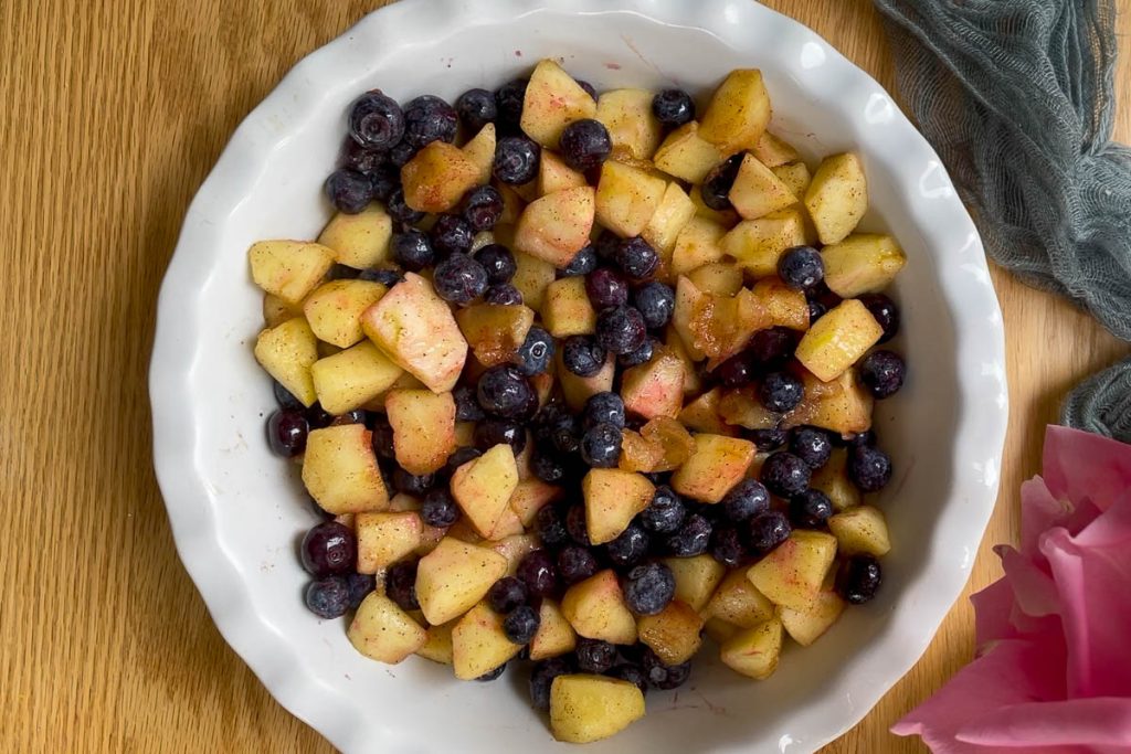 The softened apple cubes and blueberries in the bottom of a rounf dish.