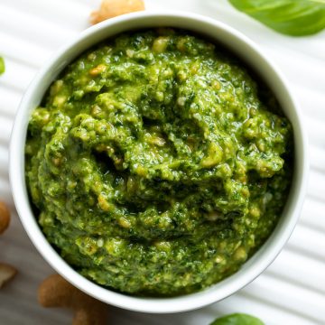 cashew pesto in a white bowl with cashews nuts and basil leaves scattered around the base.