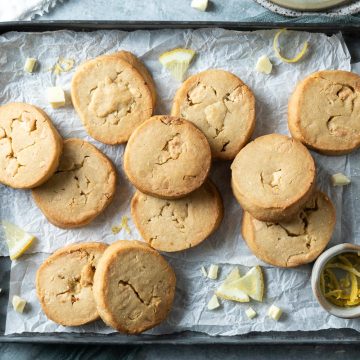 lemon white chocolate cookies on a baking tray with wedges of lemon and chunks of white chocolate