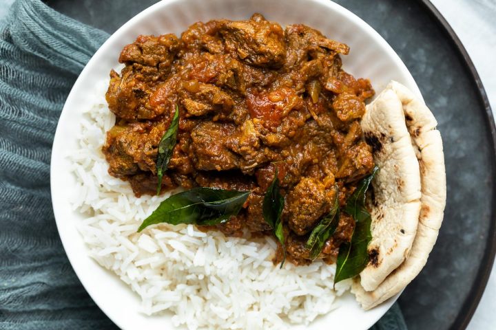 a plate of slow cooker beef madras served with rice and naan bread.