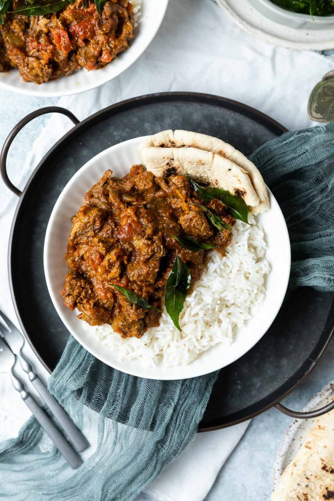 bowl of beef madras with rice, naan bread just visible on the right hand side.
