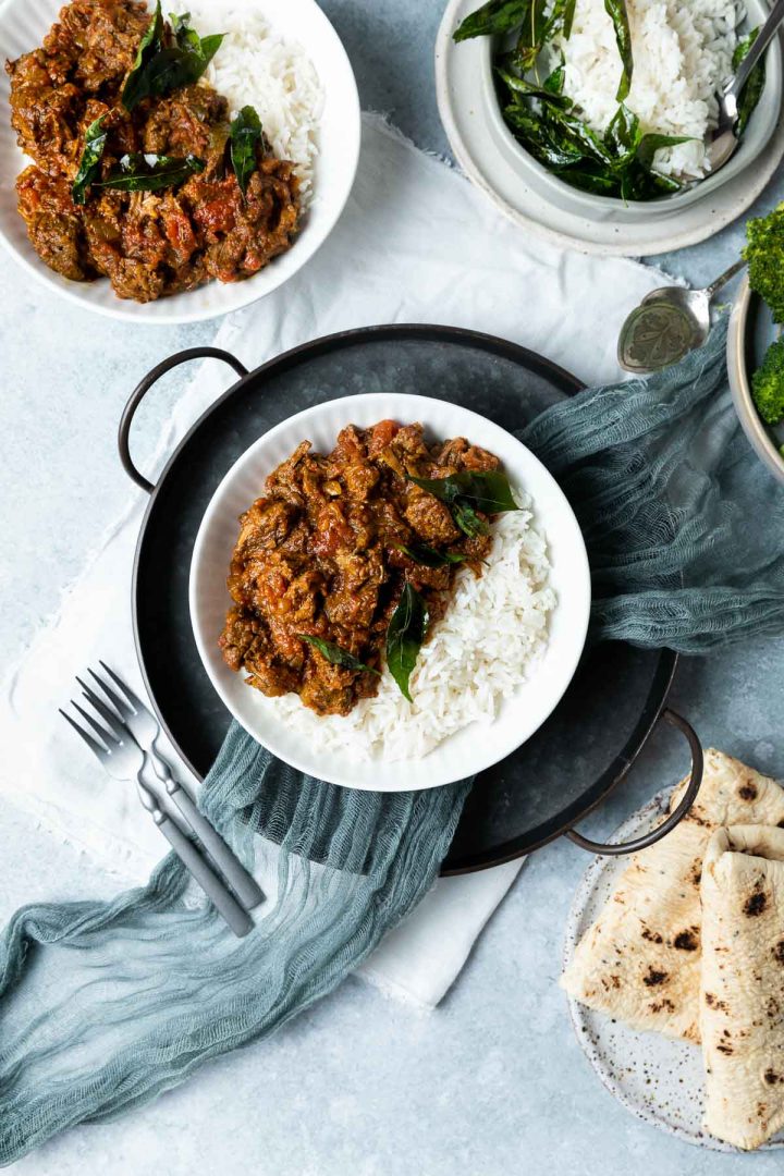 two bowls of beef madras curry served with rice, with a bowl of extra rice and plate of naan bread just visible.