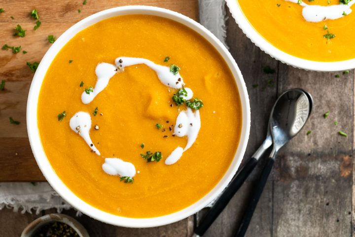slow cooker pumpkin soup in a bowl topped with a swirl of coconut milk.
