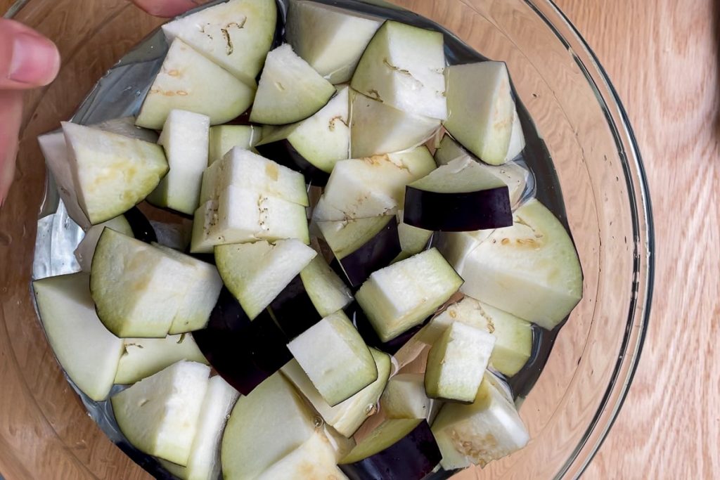 cubers of aubergine soaking in water in a bowl.