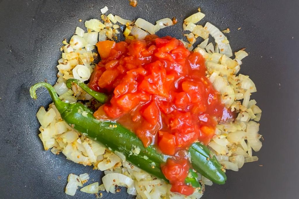 Cooked onion, green chilli and spices in a pan with tinned tomatoes added.