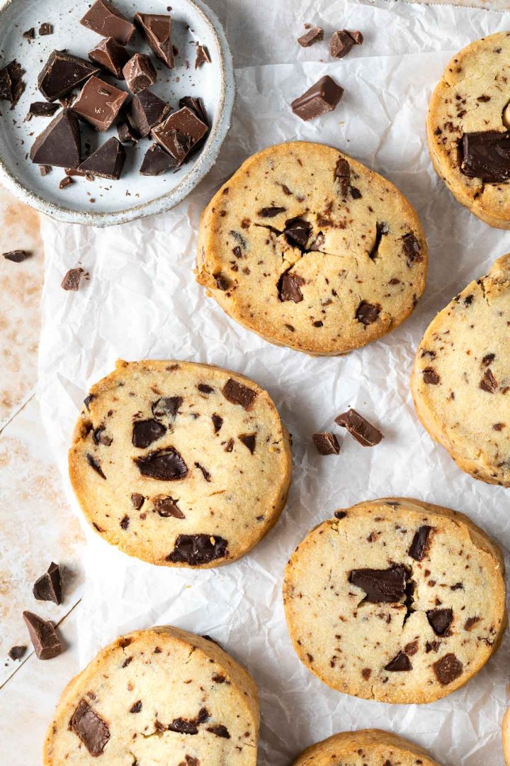 chocolate chunk cookies on a white background, with a dish of chocolate chunks in the top left corner.