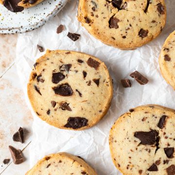 Close up of chocolate chip cookie on white background, with chocolate chunks scattered around.