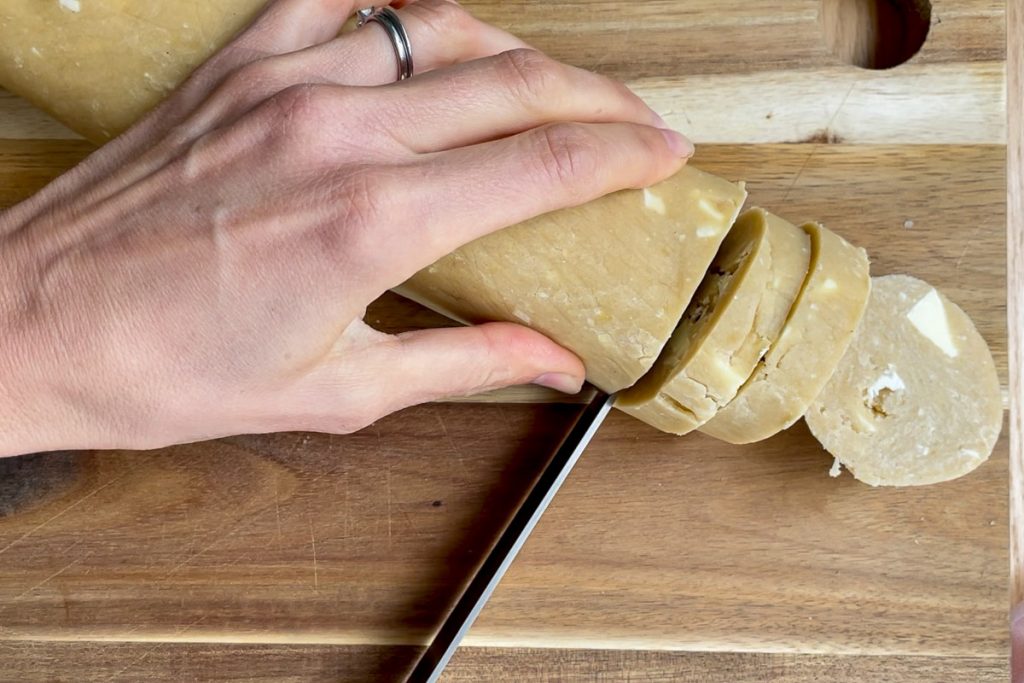 The refrigerated dough being cut on a wooden chopping board.