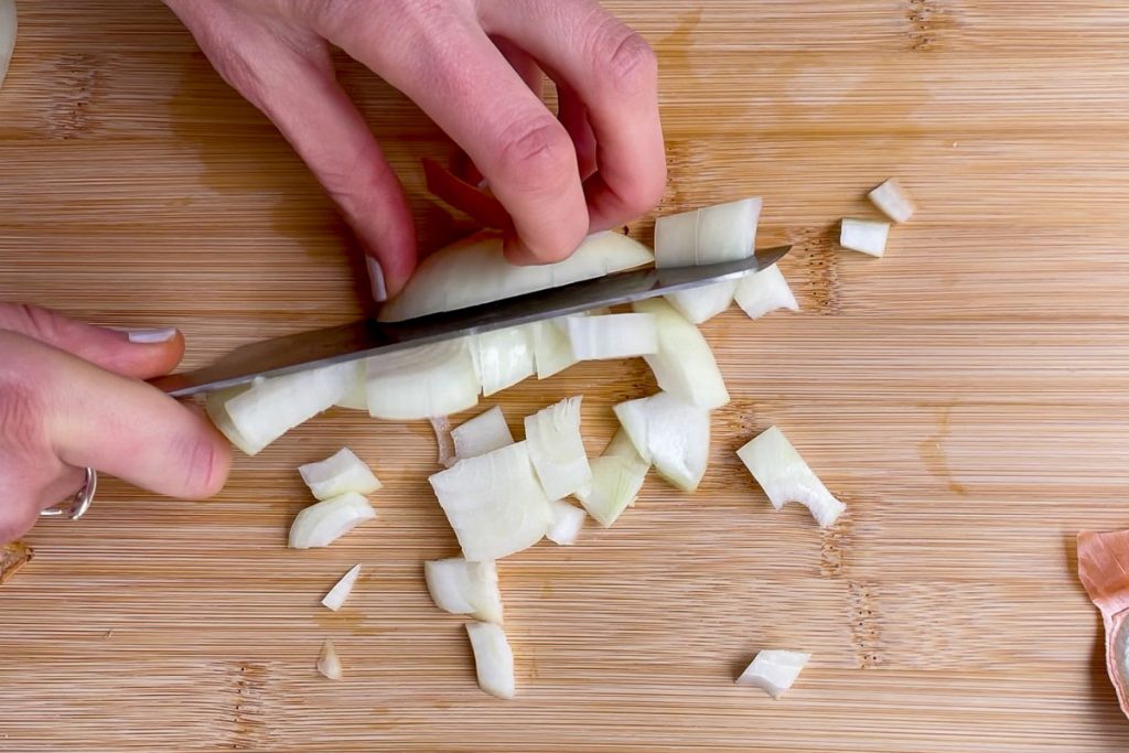 an onion being diced on a wooden chopping board.