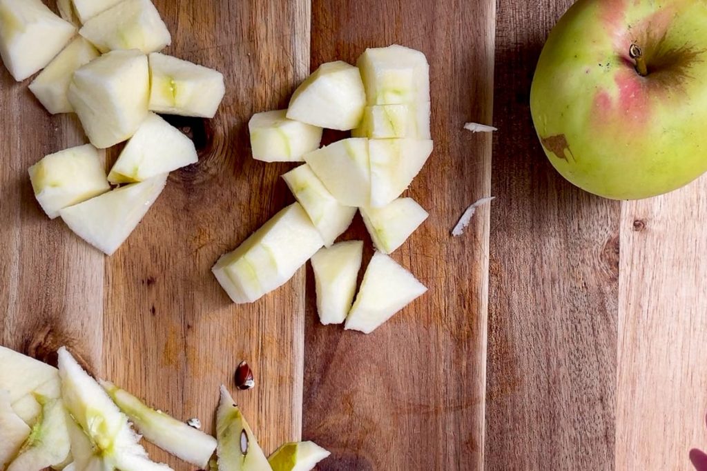 peeled and cored apples on a wooden chopping board to show the size the peices need to be.