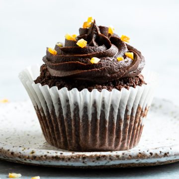 A single chocolate orange cupcake on a plate, decorated with chocolate buttercream and sprinkled with orange zest.