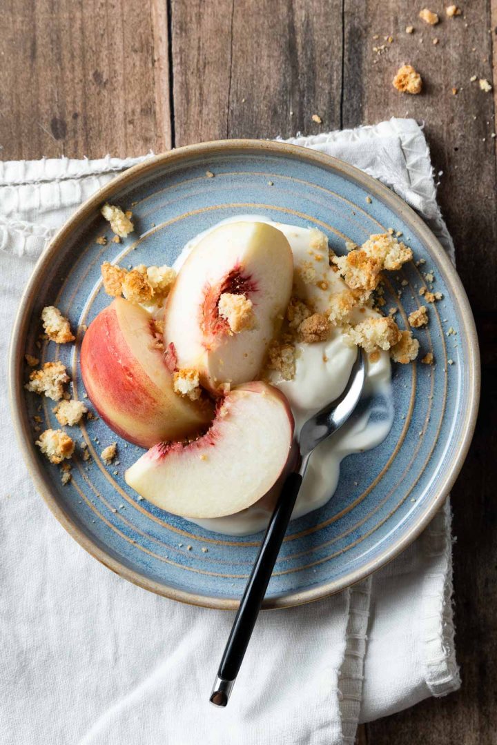a blue plate with sliced fresh peaches, yogurt and amaretti biscuits.