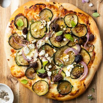 pizza topped with leftover vegetables and feta cheese on a wooden board.