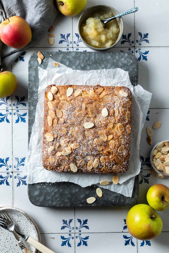 unsliced apple tray bake on a tin, with apples and apple puree just visible to the edges of the photo.