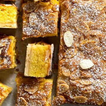 close up of apple slice, showing the icing sugar dusted top of the traybake, as well as a slice on it's side to show the layers.